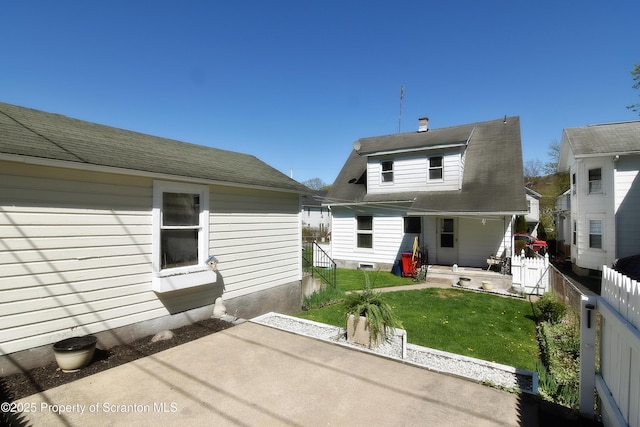 back of house featuring fence, roof with shingles, a porch, a patio area, and a lawn