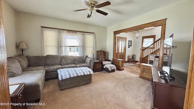 carpeted living area with ceiling fan and stairs
