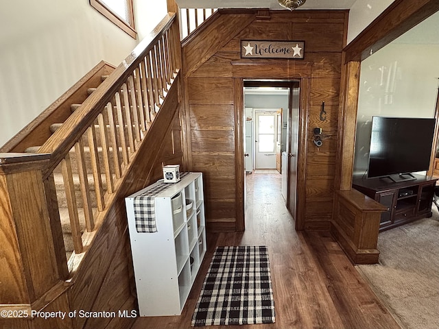 corridor with stairs, wood walls, and wood finished floors