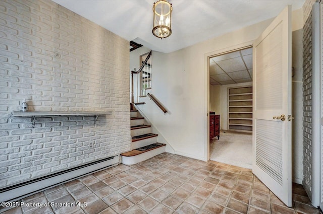 stairs featuring brick wall, a chandelier, and a baseboard radiator