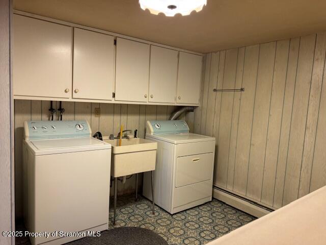 clothes washing area with a sink, cabinet space, washing machine and clothes dryer, wooden walls, and a baseboard radiator