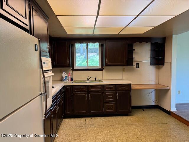 kitchen featuring freestanding refrigerator, light countertops, a sink, and dark brown cabinets