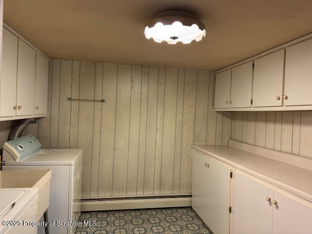 laundry room featuring washing machine and dryer, cabinet space, tile patterned flooring, a baseboard heating unit, and wooden walls