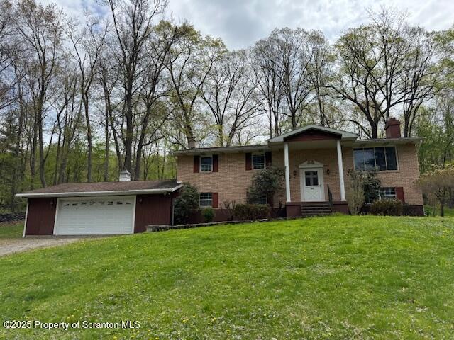 split foyer home with a chimney, brick siding, dirt driveway, an attached garage, and a front lawn