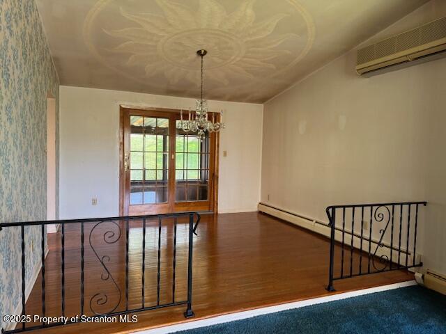 spare room with wood finished floors, an inviting chandelier, a wall unit AC, baseboards, and wallpapered walls
