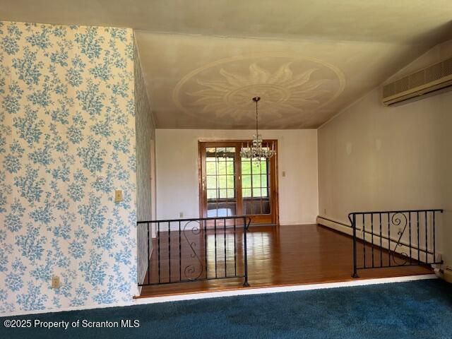 empty room featuring a chandelier, a wall unit AC, and wood finished floors