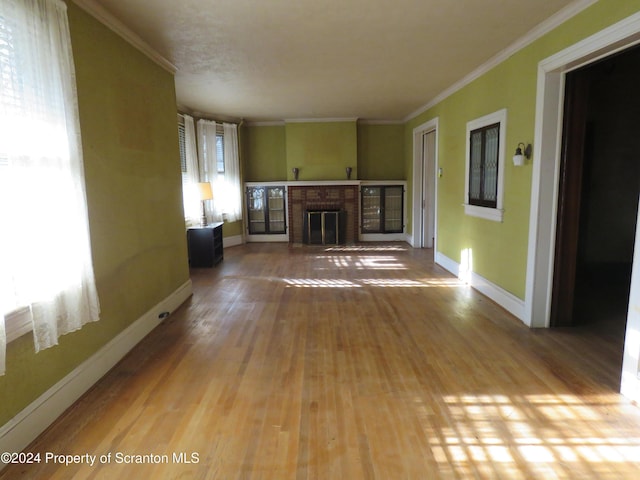 unfurnished living room featuring hardwood / wood-style flooring, a wealth of natural light, crown molding, and a fireplace