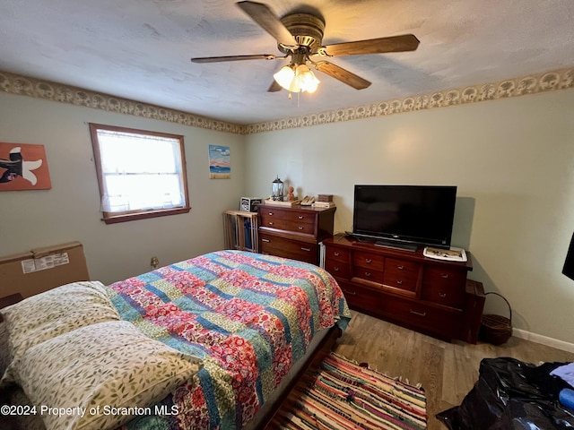 bedroom with ceiling fan, wood-type flooring, and a textured ceiling