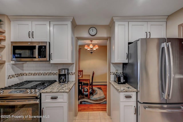 kitchen featuring decorative backsplash, light stone countertops, a notable chandelier, stainless steel appliances, and light tile patterned flooring