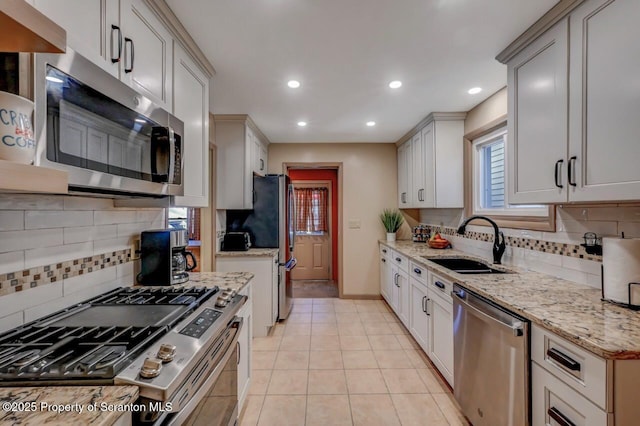 kitchen featuring light stone counters, a sink, appliances with stainless steel finishes, and tasteful backsplash