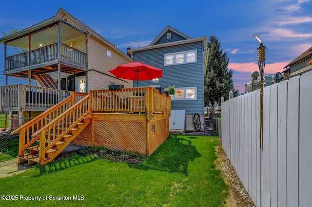 back of property at dusk with fence, stairs, a wooden deck, and a lawn