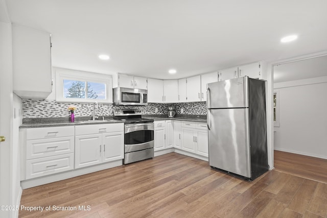 kitchen with dark countertops, appliances with stainless steel finishes, white cabinetry, a sink, and wood finished floors