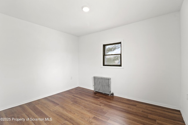 spare room featuring baseboards, dark wood finished floors, and radiator heating unit