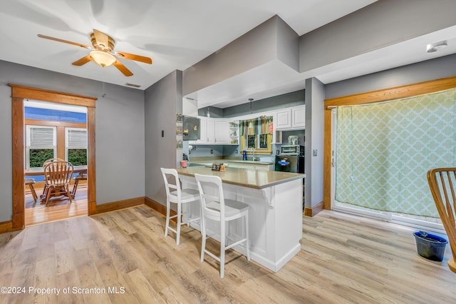 kitchen featuring kitchen peninsula, light wood-type flooring, pendant lighting, white cabinets, and a breakfast bar area