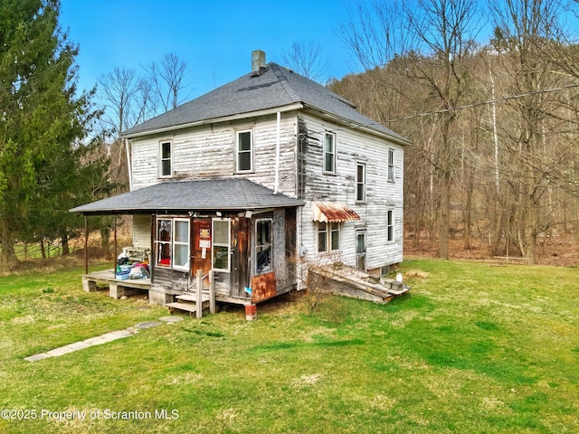 rear view of property featuring a yard and roof with shingles