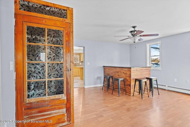 kitchen with light wood-type flooring, ceiling fan, baseboard heating, and a breakfast bar