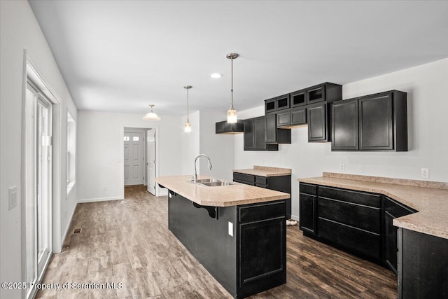 kitchen featuring dark hardwood / wood-style flooring, sink, hanging light fixtures, and a center island with sink