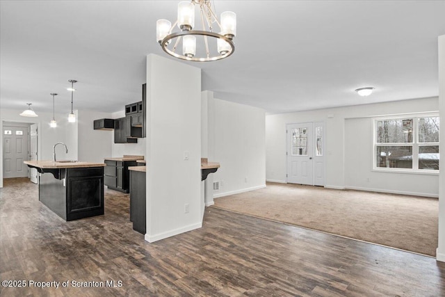 kitchen featuring sink, a breakfast bar area, a center island with sink, dark hardwood / wood-style flooring, and decorative light fixtures