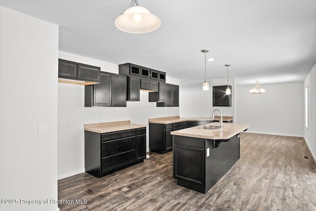 kitchen featuring decorative light fixtures, sink, dark hardwood / wood-style flooring, a notable chandelier, and a center island with sink