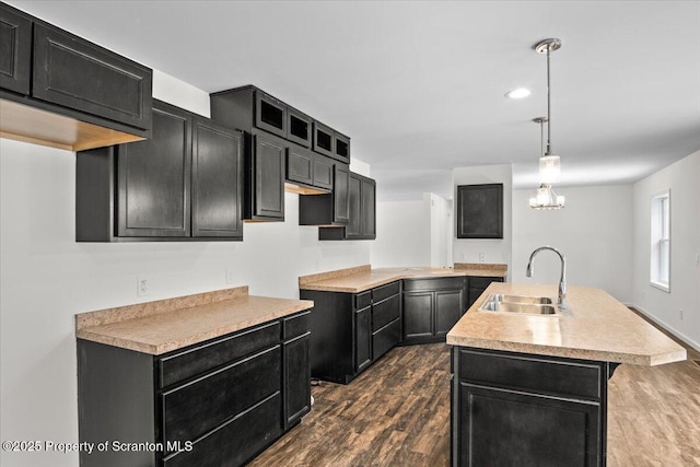 kitchen featuring an island with sink, sink, dark wood-type flooring, and decorative light fixtures