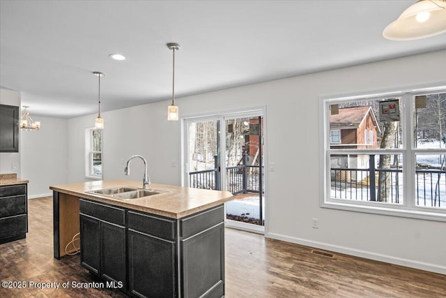 kitchen with hanging light fixtures, dark hardwood / wood-style flooring, sink, and a center island with sink