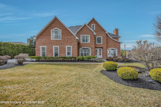 view of front of house featuring french doors, a chimney, a front lawn, and brick siding
