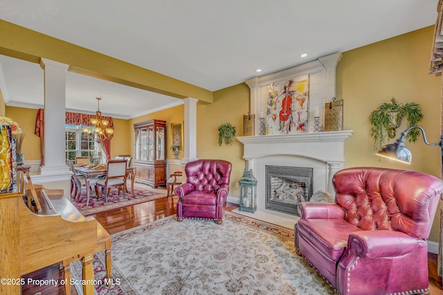 living room with a fireplace, ornate columns, an inviting chandelier, and ornamental molding