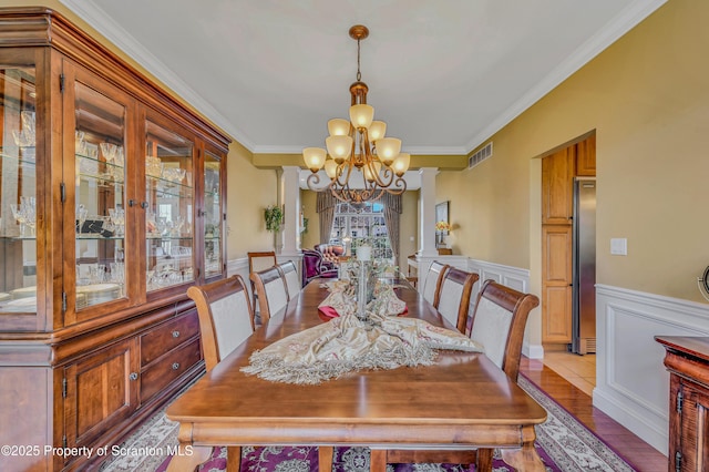 dining area with crown molding, decorative columns, visible vents, a wainscoted wall, and a chandelier