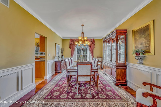 dining room with visible vents, wood finished floors, an inviting chandelier, and wainscoting