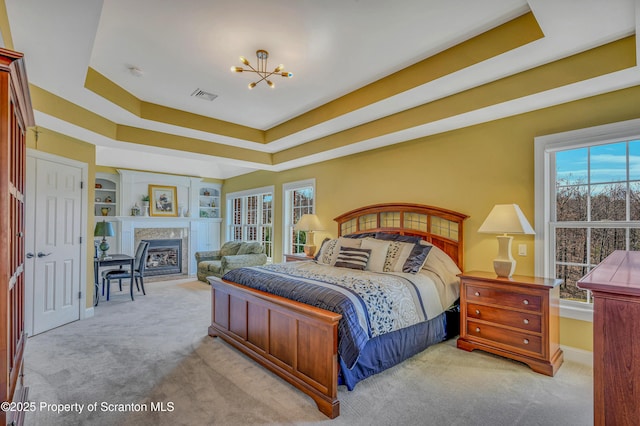 carpeted bedroom featuring a fireplace, a notable chandelier, visible vents, and a raised ceiling