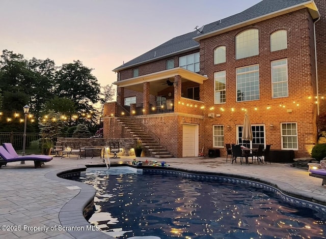 back of house at dusk featuring a fenced in pool, a patio, stairway, a ceiling fan, and brick siding