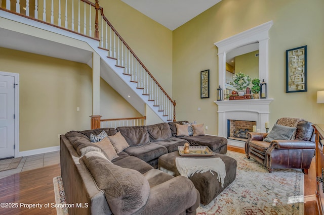 living area with a fireplace, a high ceiling, wood finished floors, stairs, and baseboards
