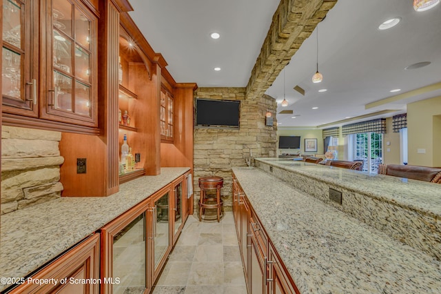 interior space featuring glass insert cabinets, hanging light fixtures, open floor plan, brown cabinets, and light stone counters
