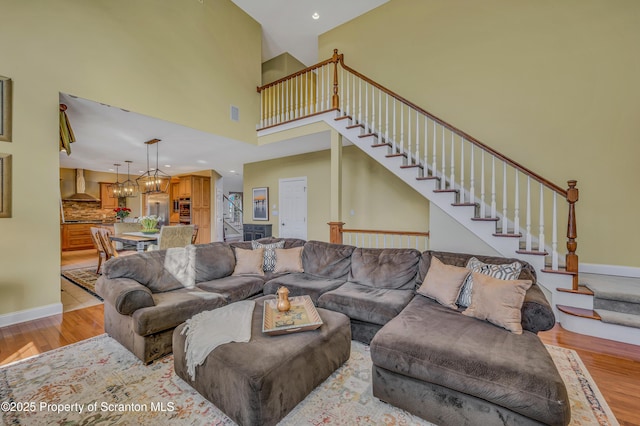 living area featuring stairway, light wood-style flooring, baseboards, and a towering ceiling