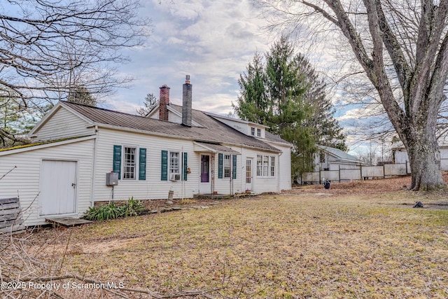rear view of house with metal roof, fence, a chimney, and a yard