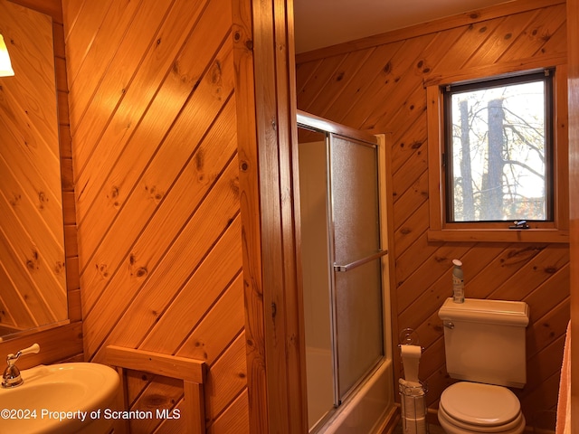 full bathroom featuring combined bath / shower with glass door, toilet, sink, and wooden walls