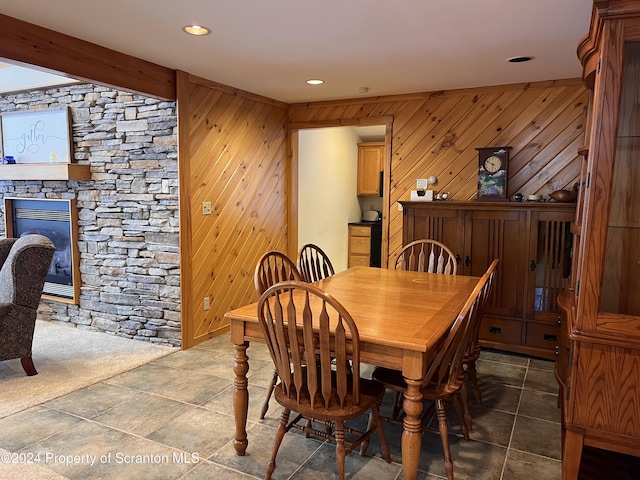 dining space with wood walls, a stone fireplace, and beam ceiling