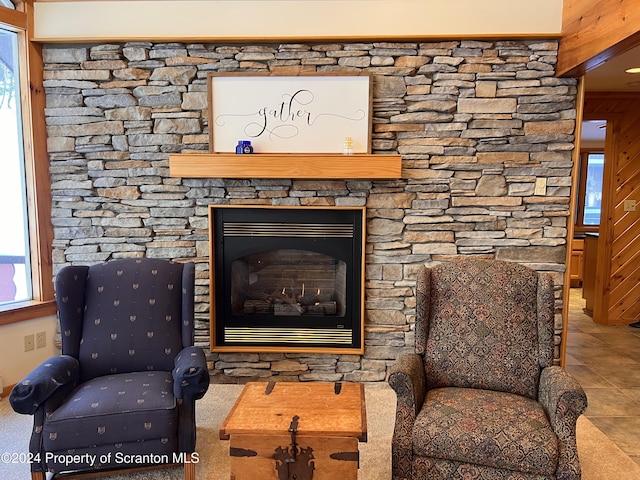 living area featuring a stone fireplace, wood walls, and light tile patterned floors