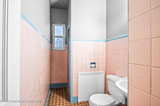 bathroom featuring toilet, wainscoting, and tile walls