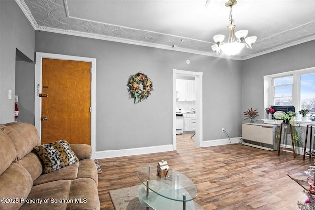 living area featuring a chandelier, ornamental molding, wood finished floors, and baseboards