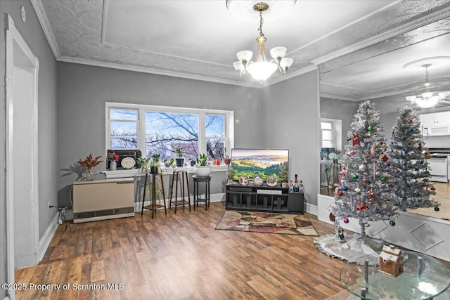 living area with crown molding, a chandelier, and wood finished floors