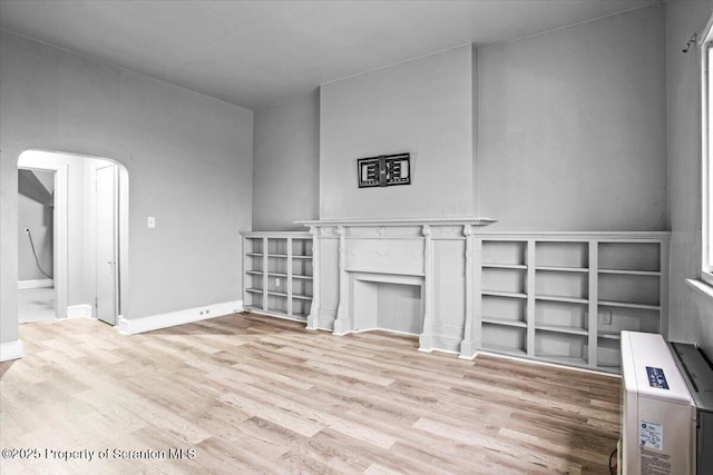 unfurnished living room with light wood-type flooring, baseboards, and arched walkways