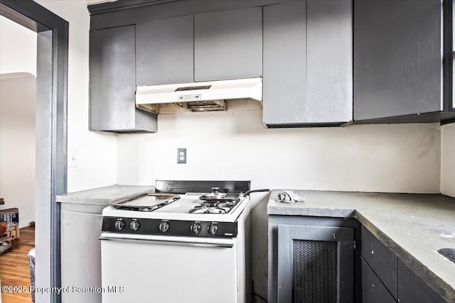 kitchen with light countertops, white gas stove, under cabinet range hood, and wood finished floors