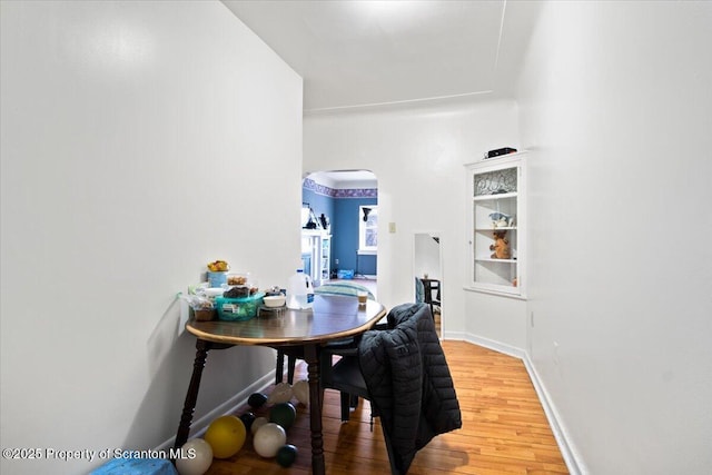 dining space featuring arched walkways, baseboards, and light wood finished floors