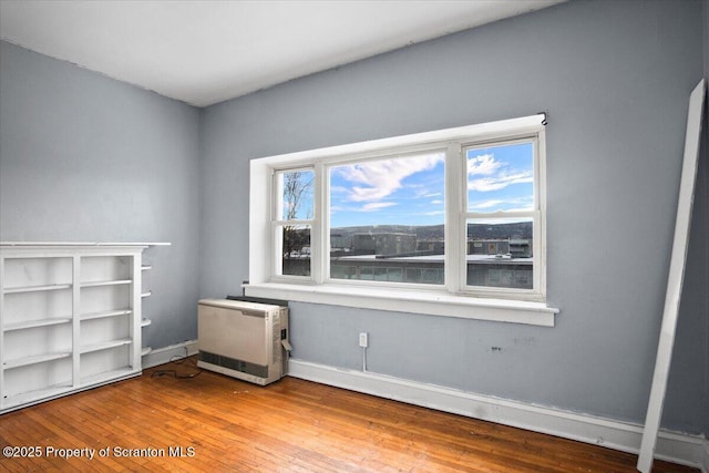 spare room featuring heating unit, hardwood / wood-style flooring, and baseboards