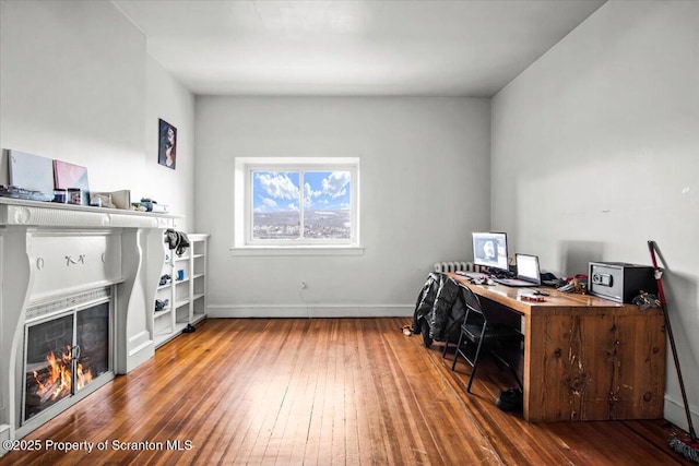 office area with a lit fireplace, wood-type flooring, and baseboards