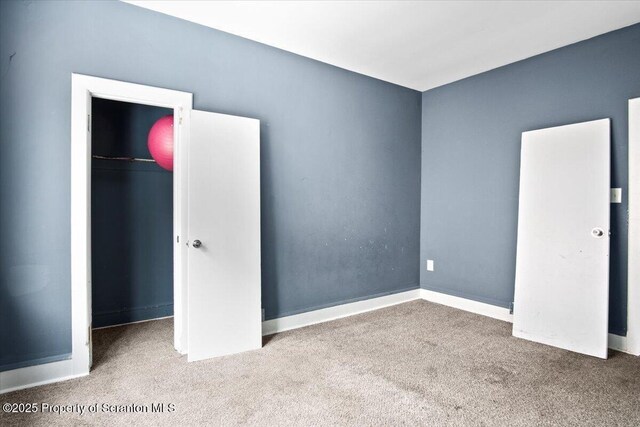 unfurnished bedroom with carpet, a spacious closet, baseboards, and a closet