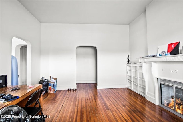 living area featuring a warm lit fireplace, baseboards, arched walkways, and hardwood / wood-style floors