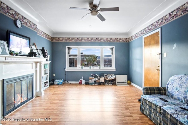 sitting room featuring a ceiling fan, a glass covered fireplace, baseboards, and hardwood / wood-style flooring