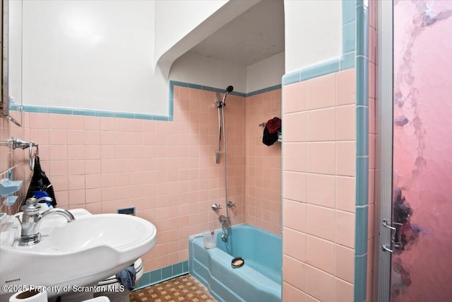 bathroom with wainscoting, shower / bath combination, a sink, and tile walls